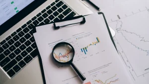 Magnifying glass over analytics report beside a laptop