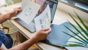person comparing two printed documents beside a laptop